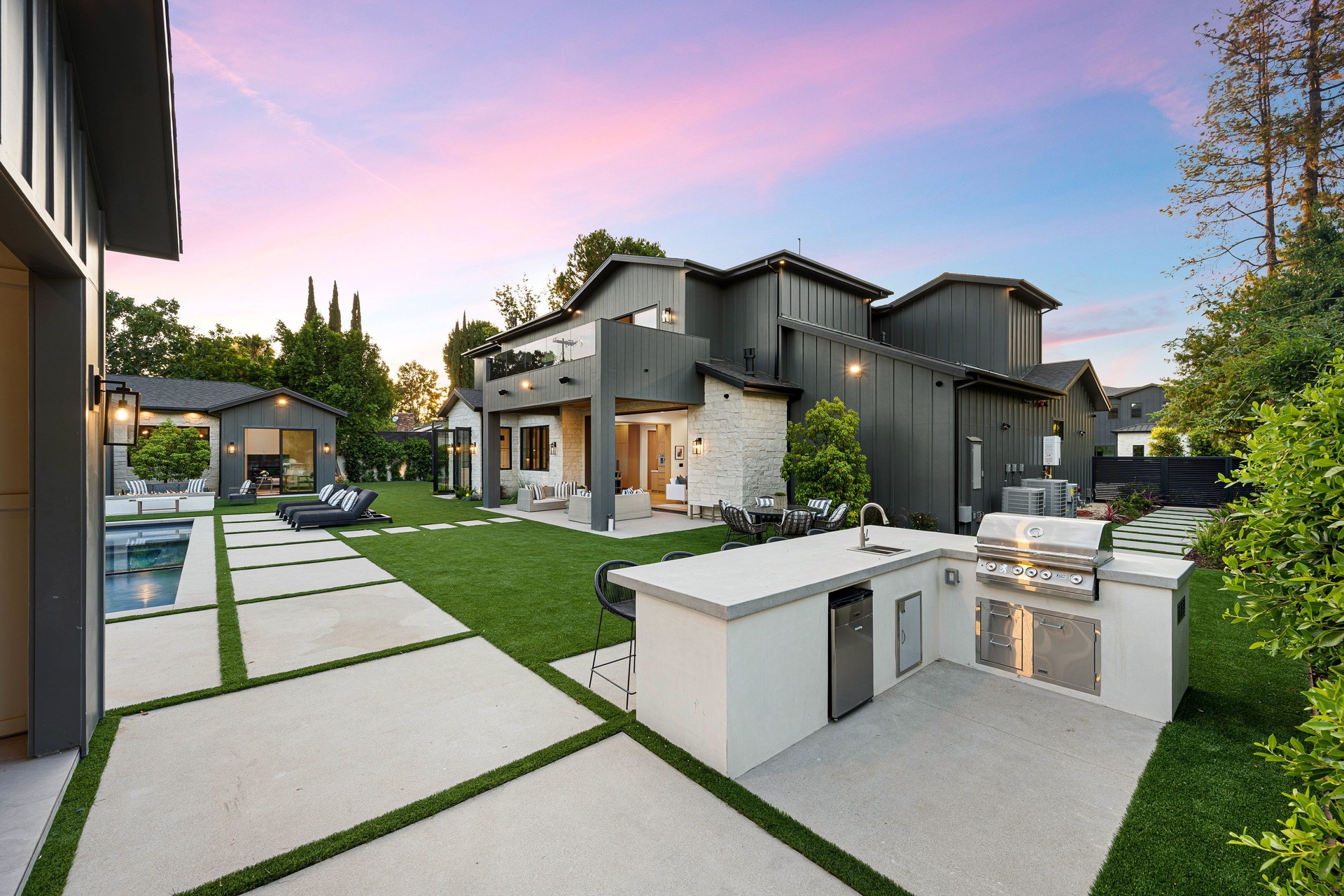 Modern backyard with outdoor kitchen and pool at sunset.